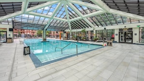 Une piscine intérieure dotée d’un toit en verre, entourée de chaises longues et d’un espace aménagé au bord de la piscine.
