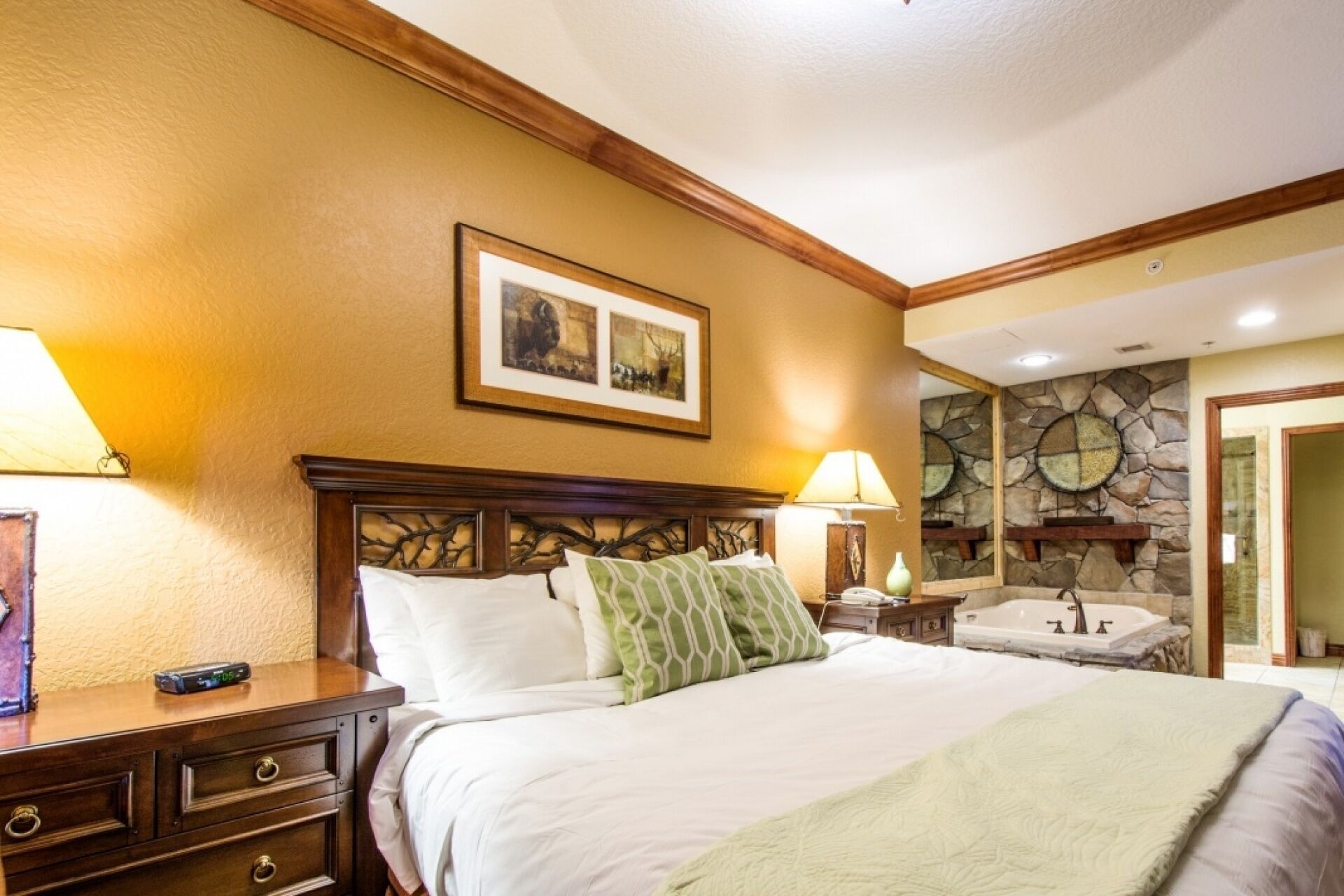 Habitación de hotel con cama, mesitas de noche, lámpara, un cuadro, pared de piedra y baño con bañera y lavamanos.