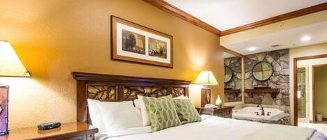 Habitación de hotel con cama, mesitas de noche, lámpara, un cuadro, pared de piedra y baño con bañera y lavamanos.