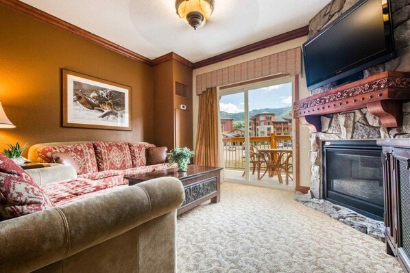 A living room with a fireplace, a sofa, a television, and a dining area with a view. - Westgate 4616 AB (Park City)