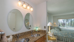 A bathroom with two sinks, a mirror, and a vanity. There is a window with a view of trees. - Gulfsands 201 · Manatee Beach · Elevator · Pool (Holmes Beach)