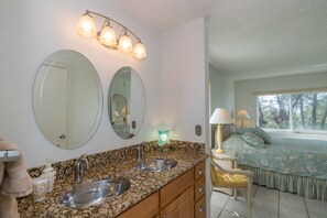 A bathroom with two sinks, a mirror, and a vanity. There is a window with a view of trees.