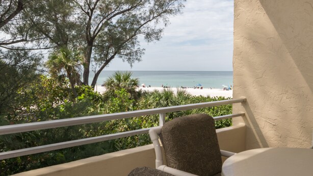 A balcony with a view of a beach, a chair, and a table. - Gulfsands 201 · Manatee Beach · Elevator · Pool (Holmes Beach)