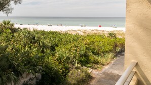 A beach view from a balcony with a path leading to the beach, surrounded by greenery. - Gulfsands 201 · Manatee Beach · Elevator · Pool (Holmes Beach)