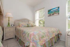 Un dormitorio con cama, mesita de noche, lámpara y un cuadro en la pared.