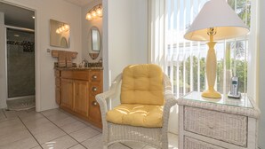 A bathroom with a wicker chair, a glass table with a lamp, and a mirror above the sink. - Gulfsands 201 · Manatee Beach · Elevator · Pool (Holmes Beach)