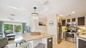 A modern kitchen with stainless steel appliances, a central island, and a dining area with bar stools. - Ground Floor Two Bedroom Island Styled Home on Beautiful Anna Maria.  Close to Beaches!! (Holmes Beach)