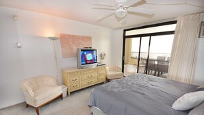 A bedroom with a bed, a television, a chair, a dresser, and a balcony with a view.