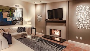 A modern living room with a sofa, coffee table, fireplace, TV, and abstract art. - Andiamo al Sole - Palm Springs Luxury Retreat (Palm Springs)