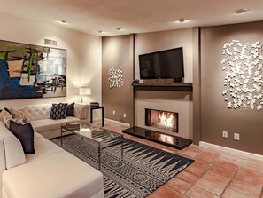 A modern living room with a sofa, coffee table, fireplace, TV, and abstract art.