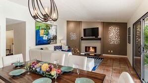 A modern living room with a fireplace, a dining table set with plates and glasses, and a large abstract painting on the wall. - Andiamo al Sole - Palm Springs Luxury Retreat (Palm Springs)