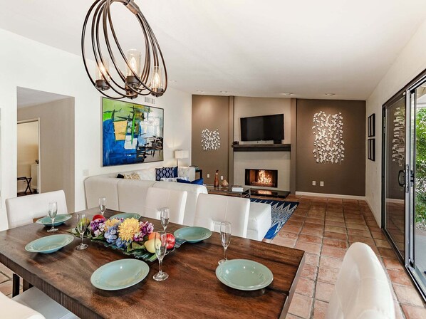 Uma sala de estar moderna com lareira, uma mesa de jantar posta com pratos e copos, e uma grande pintura abstrata na parede.