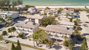 An aerial view of a coastal resort with multiple buildings, including a hotel with balconies and a beach in the background.
