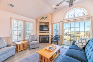 Un salon avec une cheminée, un téléviseur et un balcon donnant sur la plage.