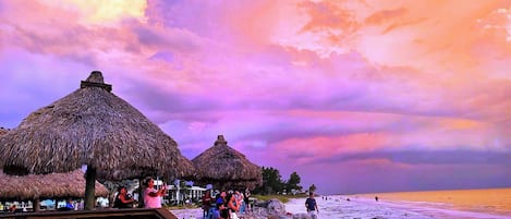 A beach with thatched-roof huts and a wooden walkway.