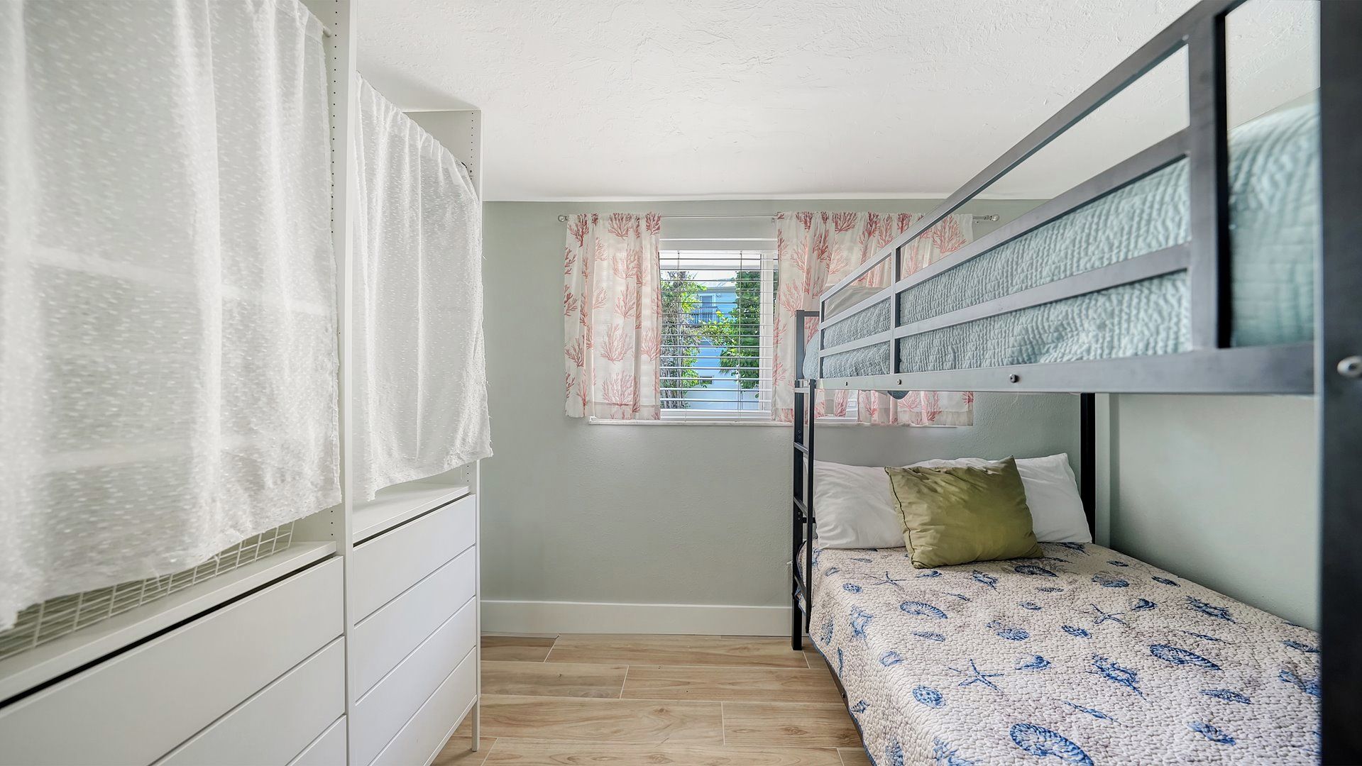 A compact bedroom with a bunk bed, a wardrobe, a window with curtains, and a view of the outside.