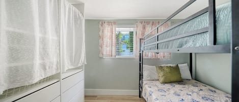 A compact bedroom with a bunk bed, a wardrobe, a window with curtains, and a view of the outside.