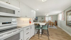 A modern kitchen with white cabinetry, a built-in microwave, and a dining area with wooden chairs and a table.