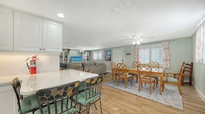 A modern kitchen with white cabinets, a dining area with wooden chairs and a glass table, and a ceiling fan.
