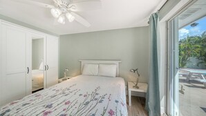 A bedroom with a bed, bedside lamps, a ceiling fan, and a view of the outdoors. - 4BR Coastal Cottage w/ Heated Private Pool | 1 Block to Bean Point Beach | Dog Friendly *(See Note) ! (Anna Maria)