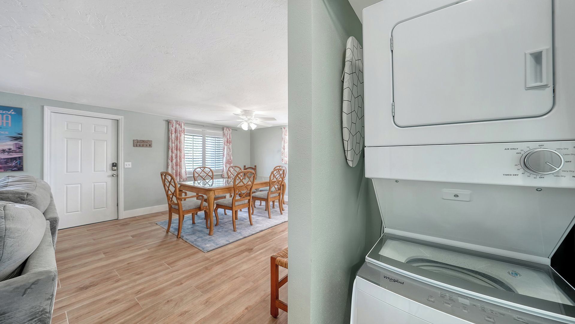Un salon avec un canapé gris, un coin repas avec une table et des chaises, et un espace buanderie équipé d’un lave-linge et d’un sèche-linge Whirlpool.