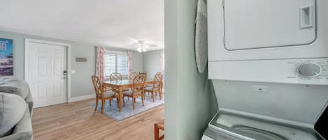 Una sala de estar con un sofá gris, un comedor con mesa y sillas, y un área de lavandería con lavadora y secadora Whirlpool.