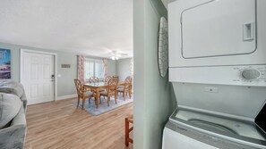 Ein Wohnzimmer mit grauem Sofa, ein Essbereich mit Tisch und Stühlen sowie eine Waschküche mit Whirlpool Waschmaschine und Trockner.