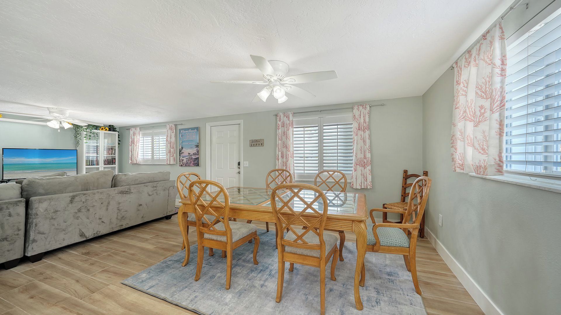 A living room with a sofa, a dining table with chairs, a ceiling fan, and a TV.