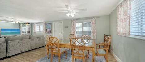 A living room with a sofa, a dining table with chairs, a ceiling fan, and a TV.