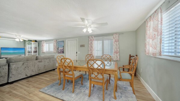 A living room with a sofa, a dining table with chairs, a ceiling fan, and a TV.