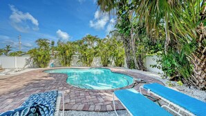 A swimming pool with a brick deck, surrounded by tropical plants and a white fence. - 4BR Coastal Cottage w/ Heated Private Pool | 1 Block to Bean Point Beach | Dog Friendly  *(See Note) ! (Anna Maria)
