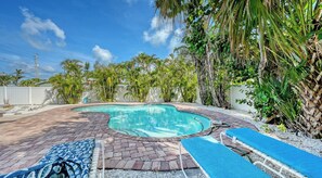 Une piscine entourée d’une terrasse en briques, de plantes tropicales et d’une clôture blanche.
