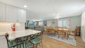 A modern kitchen with white cabinets, a dining area with wooden chairs and a glass table, and a ceiling fan. - 4BR Coastal Cottage w/ Heated Private Pool | 1 Block to Bean Point Beach | Dog Friendly  *(See Note) ! (Anna Maria)