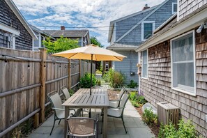 Une terrasse avec une table et des chaises, une clôture en bois et une maison avec un revêtement extérieur et des fenêtres.