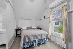 Une chambre à coucher avec un lit, des tables de chevet, une fenêtre avec des rideaux et un ventilateur de plafond.
