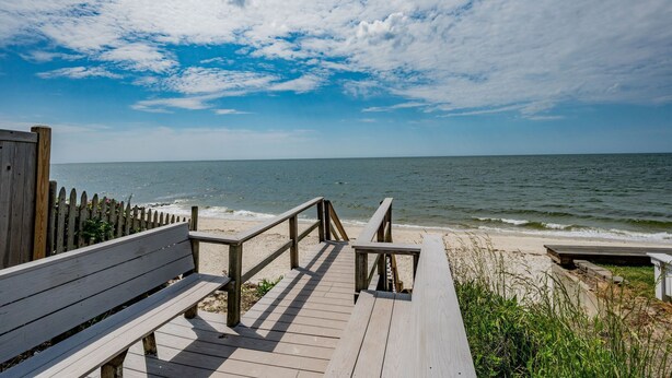 A wooden boardwalk leading to a beach with a wooden fence and benches.