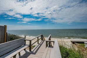 Une promenade en bois menant à une plage, avec une clôture en bois et des bancs.