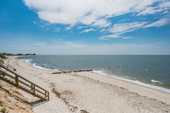 Une plage avec une promenade en bois menant à l’eau, un ciel dégagé et des bâtiments situés au loin.