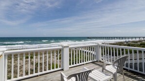 A wooden deck with white railings overlooking a beach and a pier.