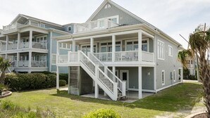 A two-story residential building with a balcony on the upper floor, a staircase leading to the entrance, and a well-maintained lawn.