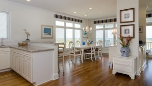 A spacious kitchen with a large island, white cabinetry, and a dining area with chairs and a table.