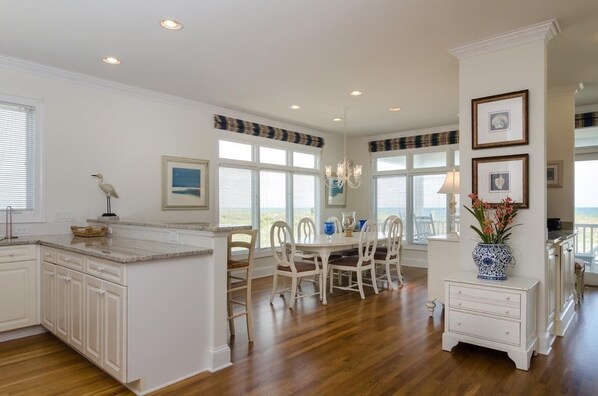A spacious kitchen with a large island, white cabinetry, and a dining area with chairs and a table.