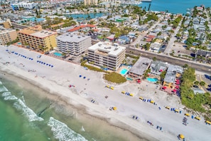 An aerial view of a coastal city with a beach, hotels, and a marina.