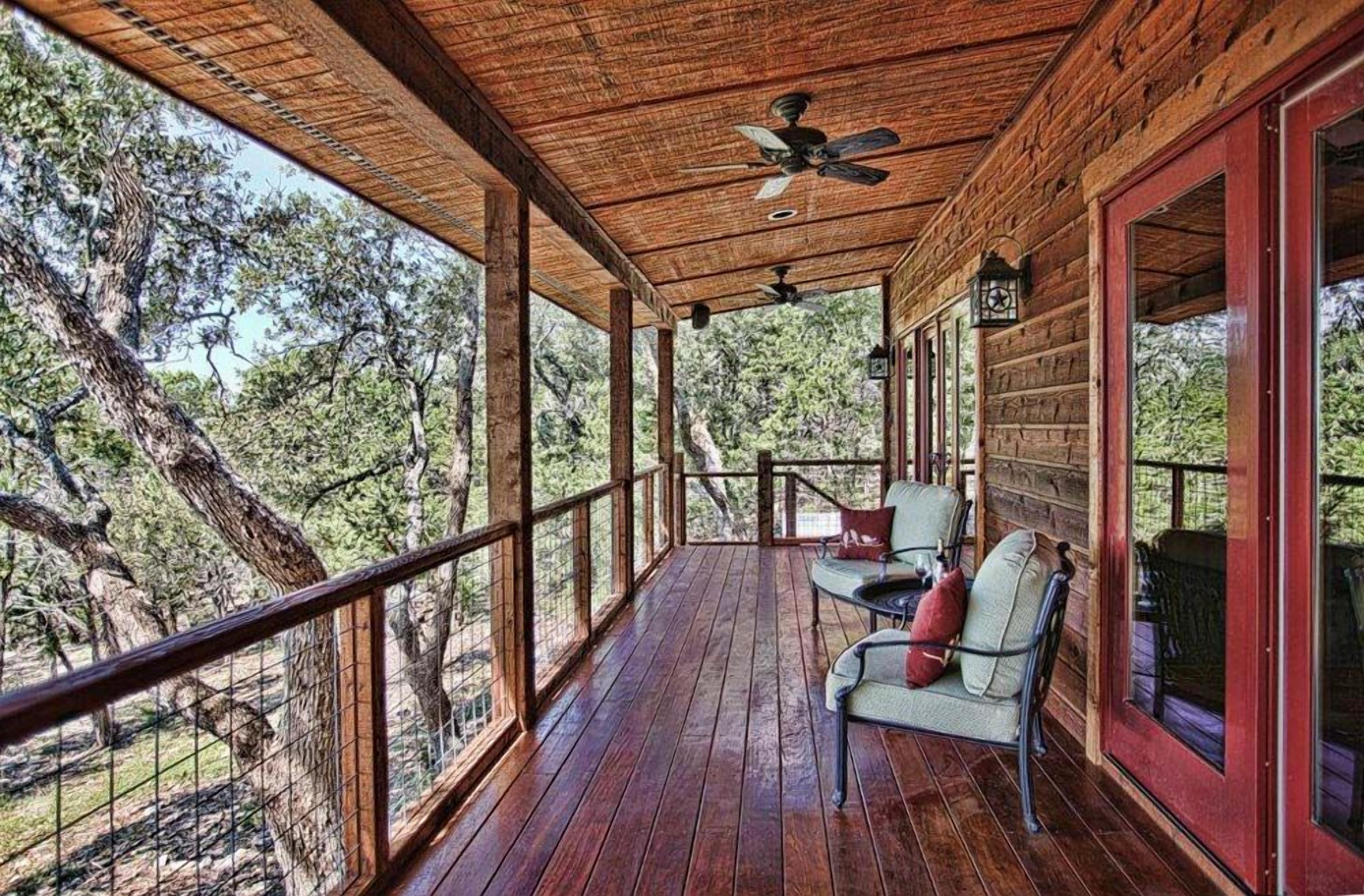 Una terraza de madera con barandilla, dos sillas y una mesa.