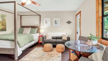 A bedroom with a four-poster bed, a sofa, a glass table, and a window with a view.