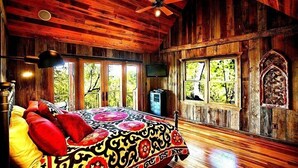 A wooden cabin bedroom with a bed, a ceiling fan, and large windows. - Upscale Luxury Cabin! Has it all Hot tub, Fireplace, Gorgeous Views!!! (Wimberley)