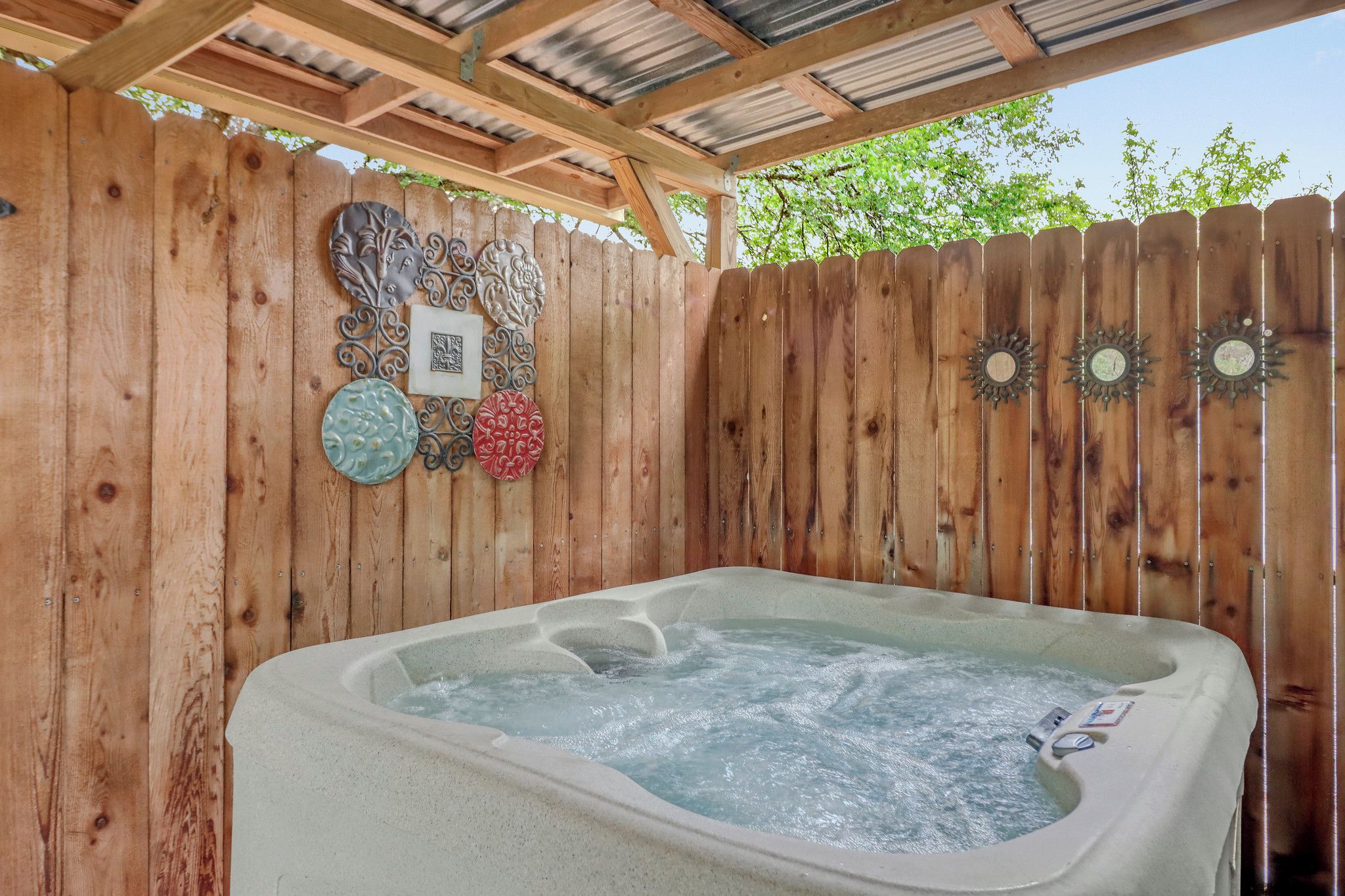 A hot tub under a wooden pergola with decorative wall art.