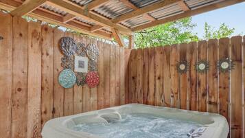 A hot tub under a wooden pergola with decorative wall art.
