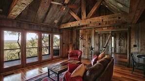 A rustic interior with wooden beams, a leather sofa, and large windows overlooking a landscape. - Upscale Luxury Cabin! Has it all Hot tub, Fireplace, Gorgeous Views!!! (Wimberley)