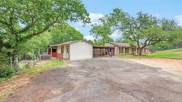 A two-story house with a covered porch, a garage, and a driveway leading to a grassy area.